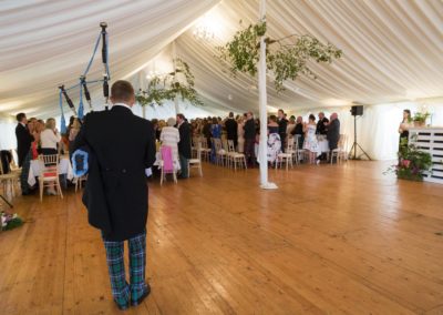 The wedding piper playing bagpipes inside a wedding marquee hire in Scotland
